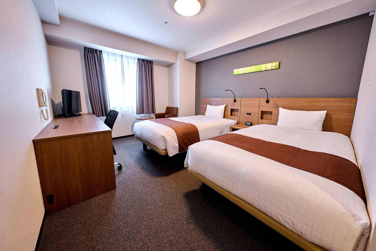 A hotel room with two beds, a desk, a chair, a TV, and a phone.