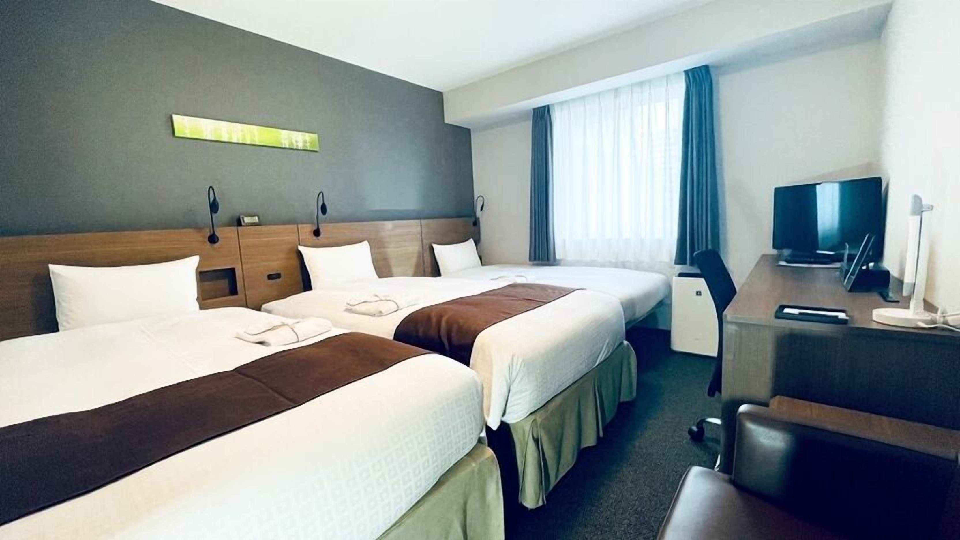 A hotel room with two beds, a desk, a television, and a window with curtains.