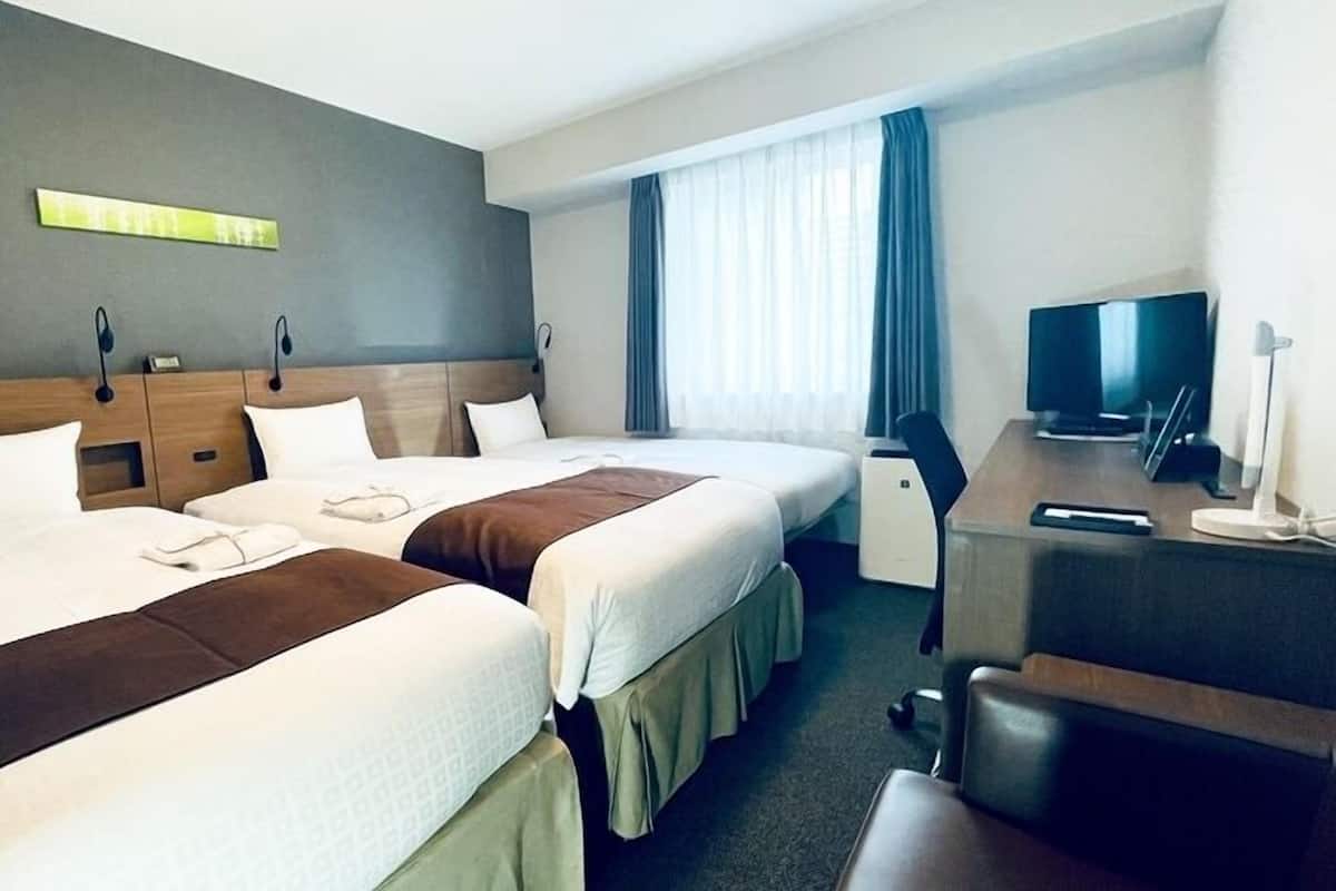 A hotel room with two beds, a desk, a television, and a window with curtains.