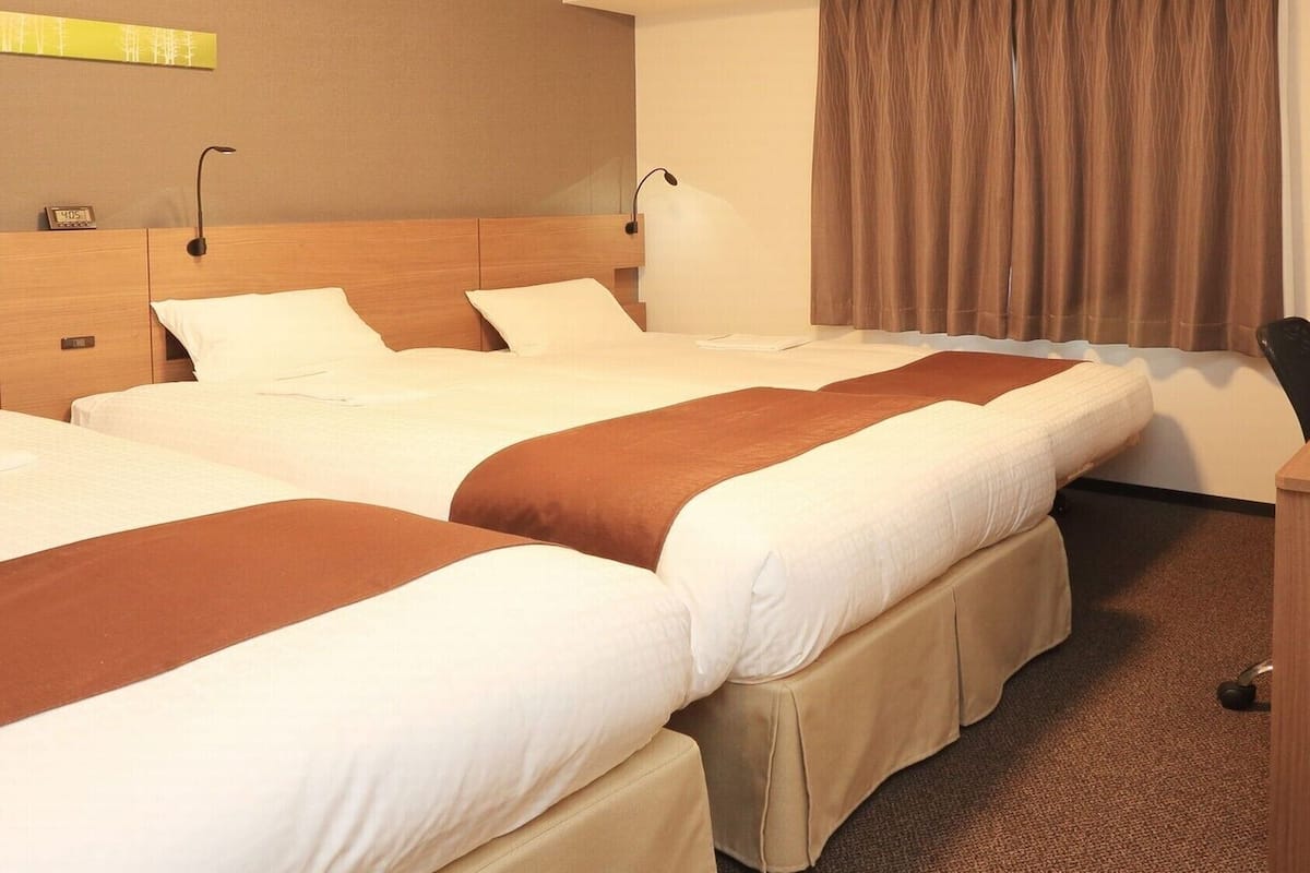 Hotellihuone, jossa on kolme sänkyä, työpöytä ja tuoli.