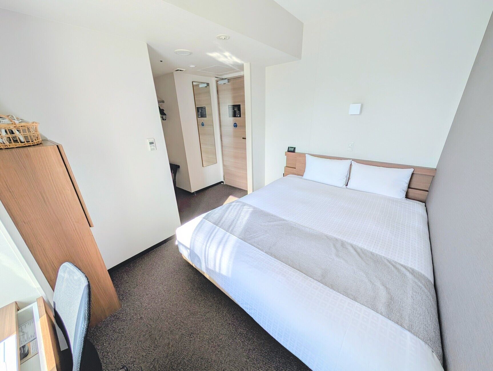 A hotel room with a bed, a wooden wardrobe, a desk, and a chair.