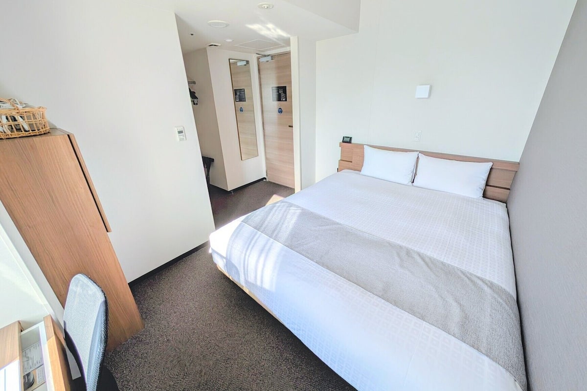 A hotel room with a bed, a wooden wardrobe, a desk, and a chair.