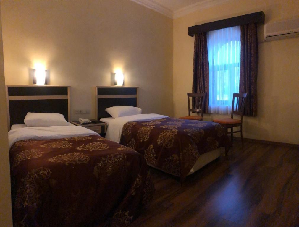A hotel room with two beds, a chair, a nightstand, and a window with curtains.
