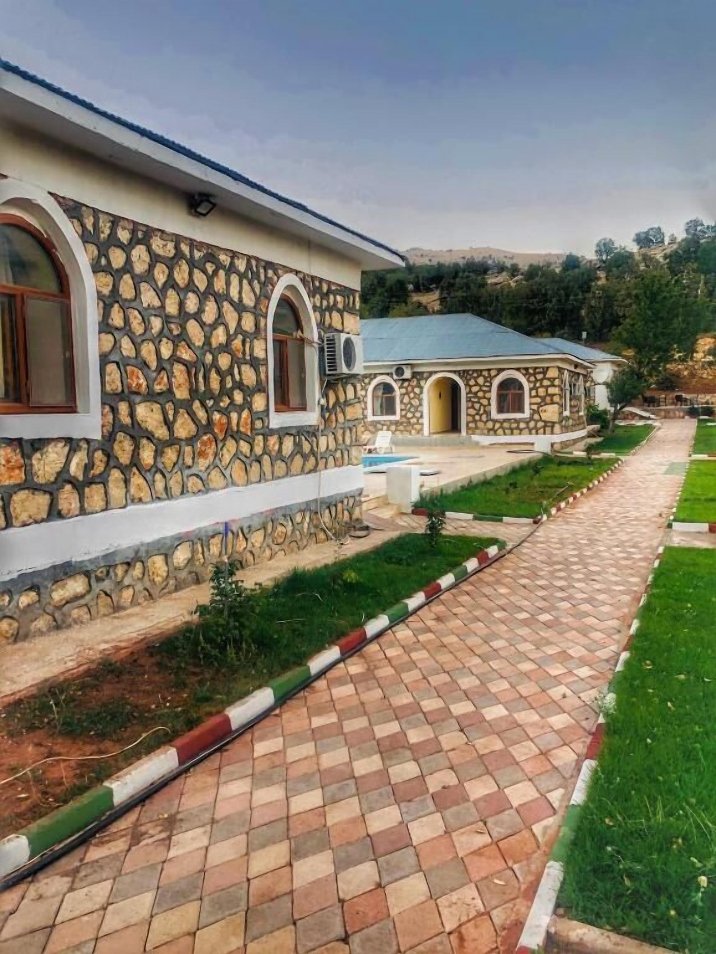A stone building with a paved walkway leading to a pool area.