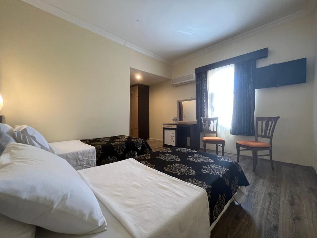 A hotel room with two beds, a desk, a chair, and a window.