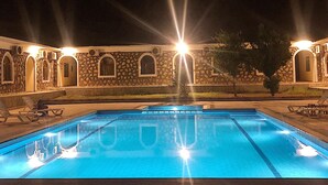 A swimming pool with clear blue water, surrounded by stone walls and arched windows. - Nemrut Euphrat Hotel (Kahta)