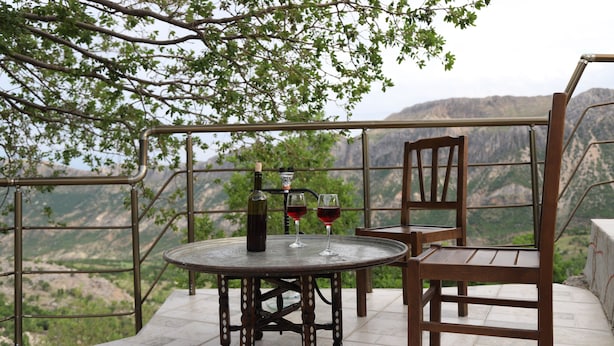 A round metal table with two wine glasses and a bottle, a wooden chair, and a metal railing overlooking a mountainous landscape. - Nemrut Euphrat Hotel (Kahta)
