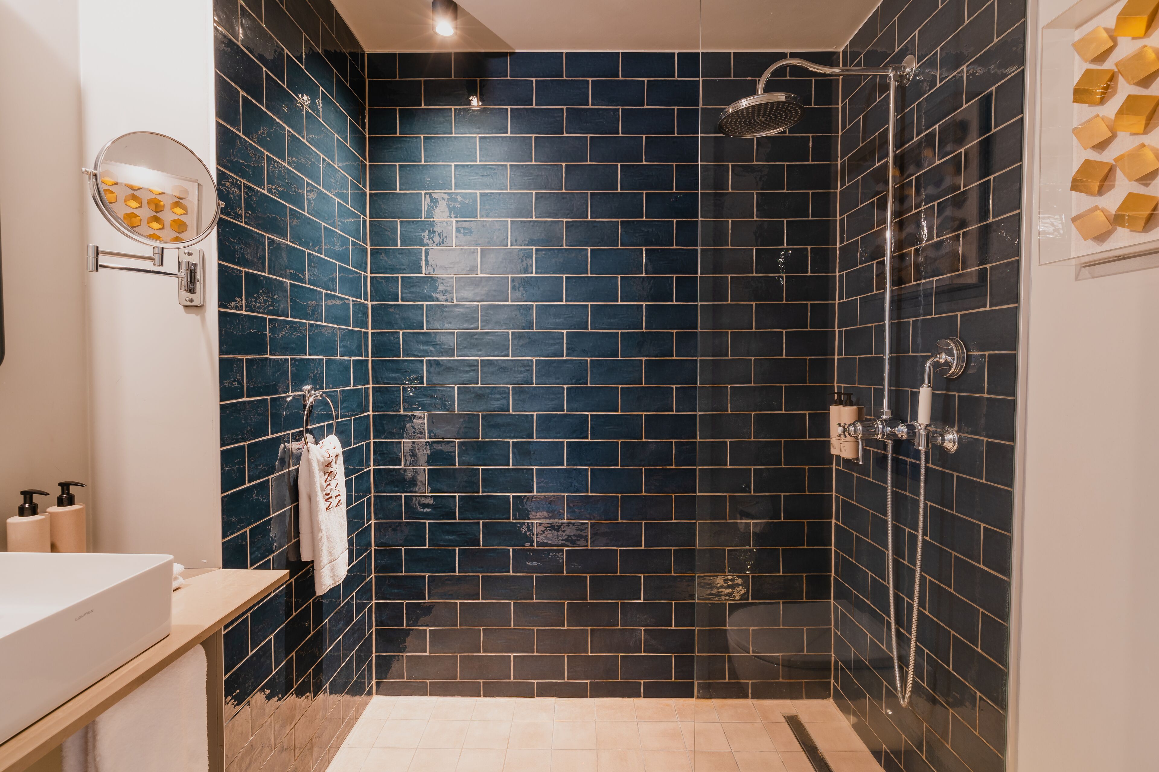 Une salle de bain avec des murs recouverts de carreaux bleu foncé, un lavabo blanc et une douche à parois de verre.