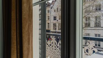 A view from a window with a curtain, featuring a balcony with ornate white railings and a building with multiple windows in the background.