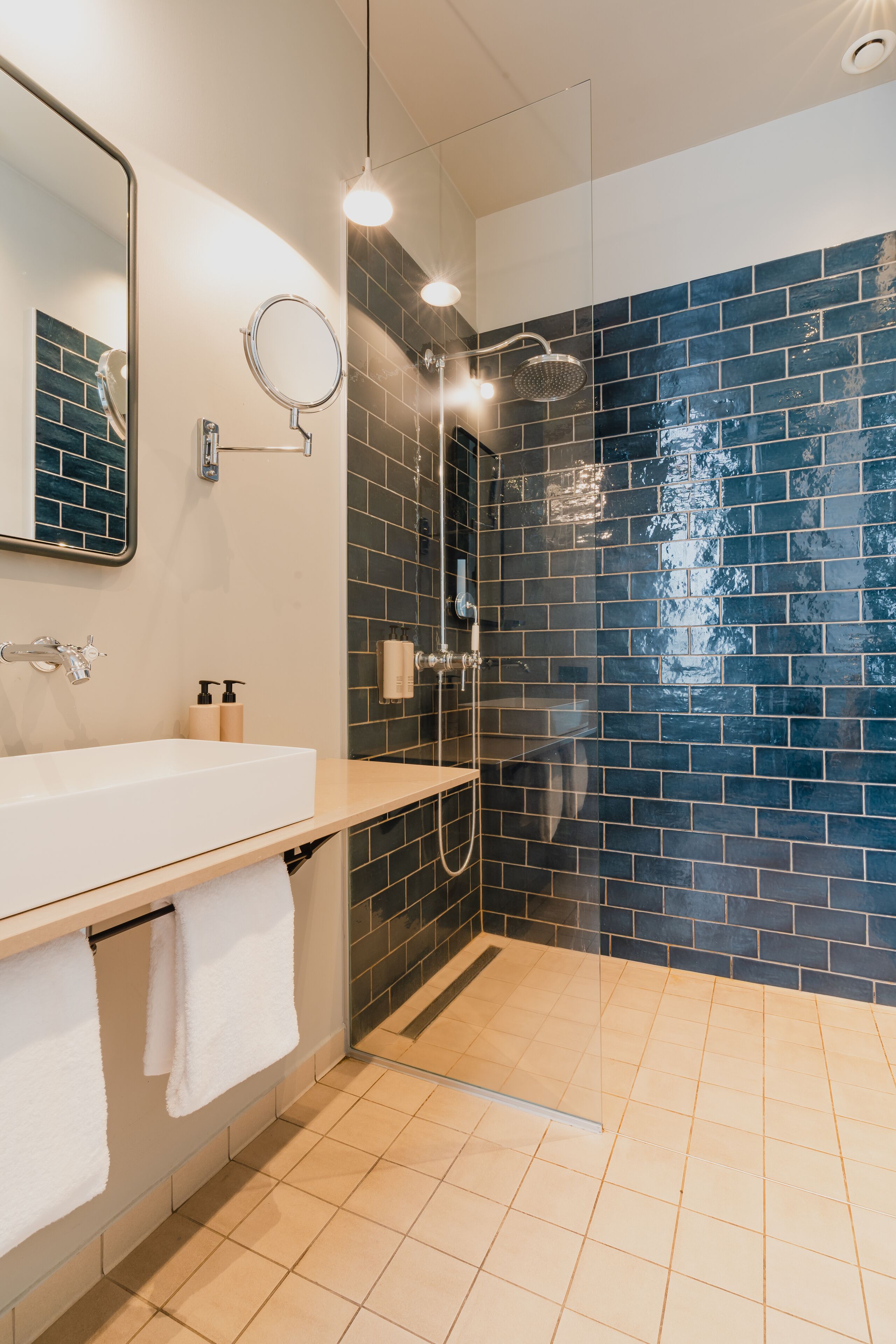 Un baño moderno con un lavamanos blanco, un espejo y una zona de ducha con paredes de vidrio y azulejos azules.