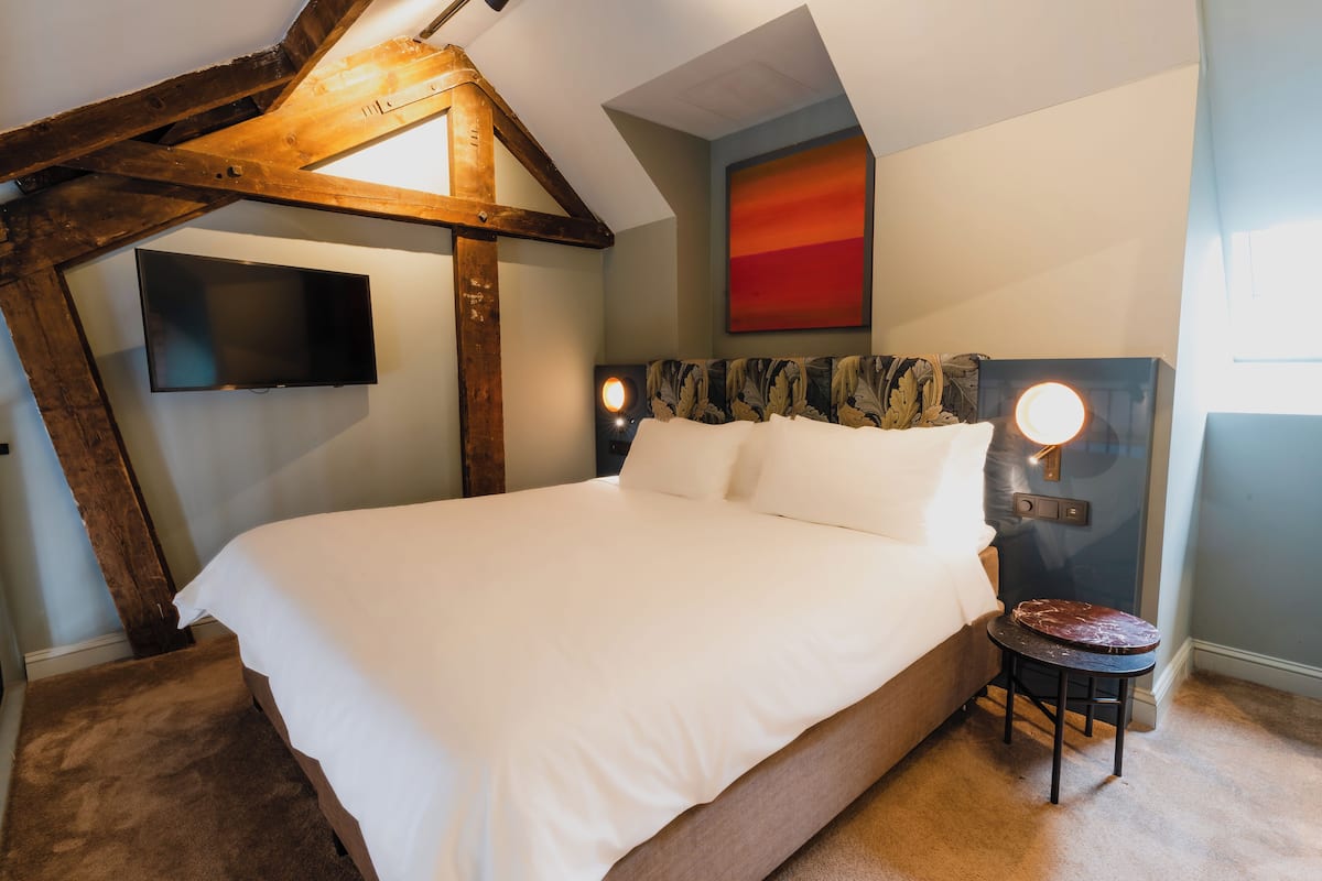 Une chambre dotée d’un grand lit, d’un téléviseur fixé au mur, d’un décor de plafond original et d’un tableau représentant un coucher de soleil rouge.