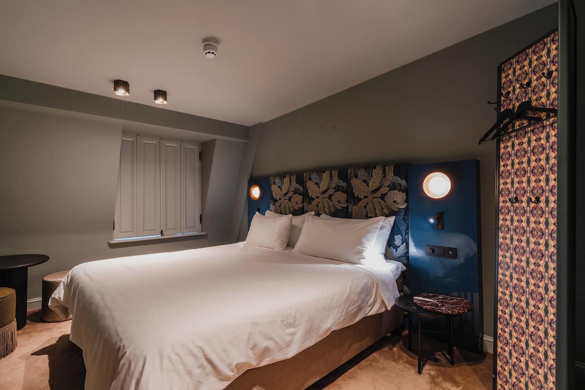 Une chambre avec un grand lit, une petite table, une chaise et une fenêtre avec des rideaux.