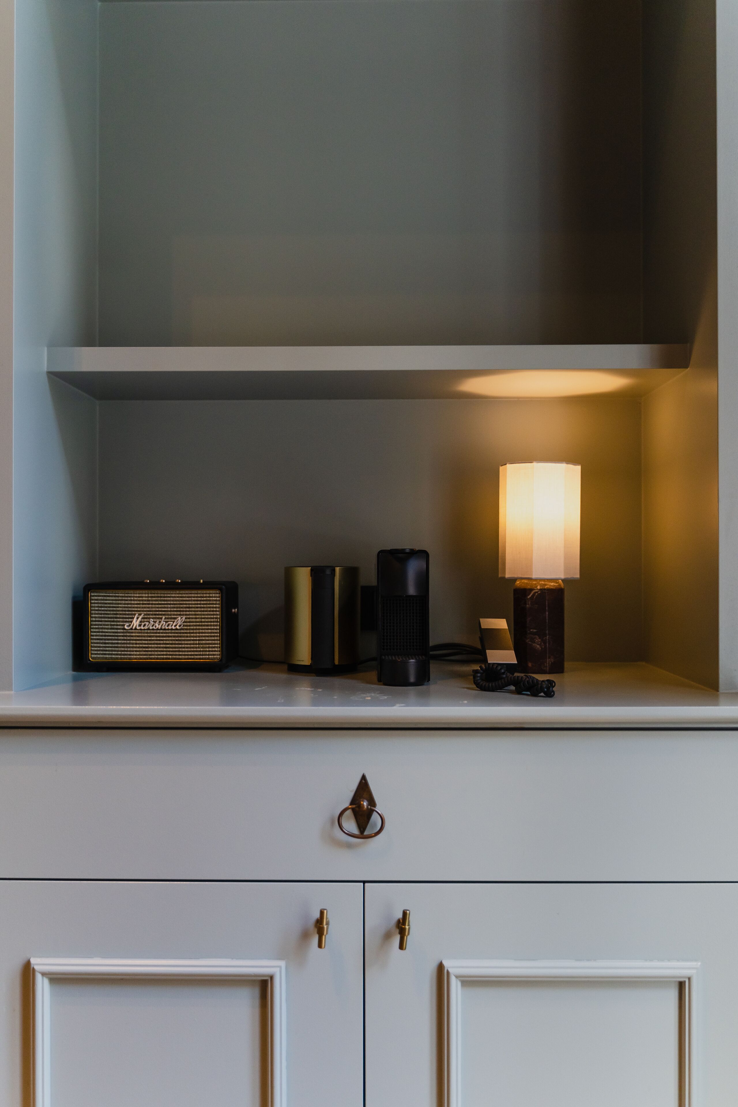 Una estantería con una radio antigua, un altavoz moderno, una lámpara y un pequeño adorno.