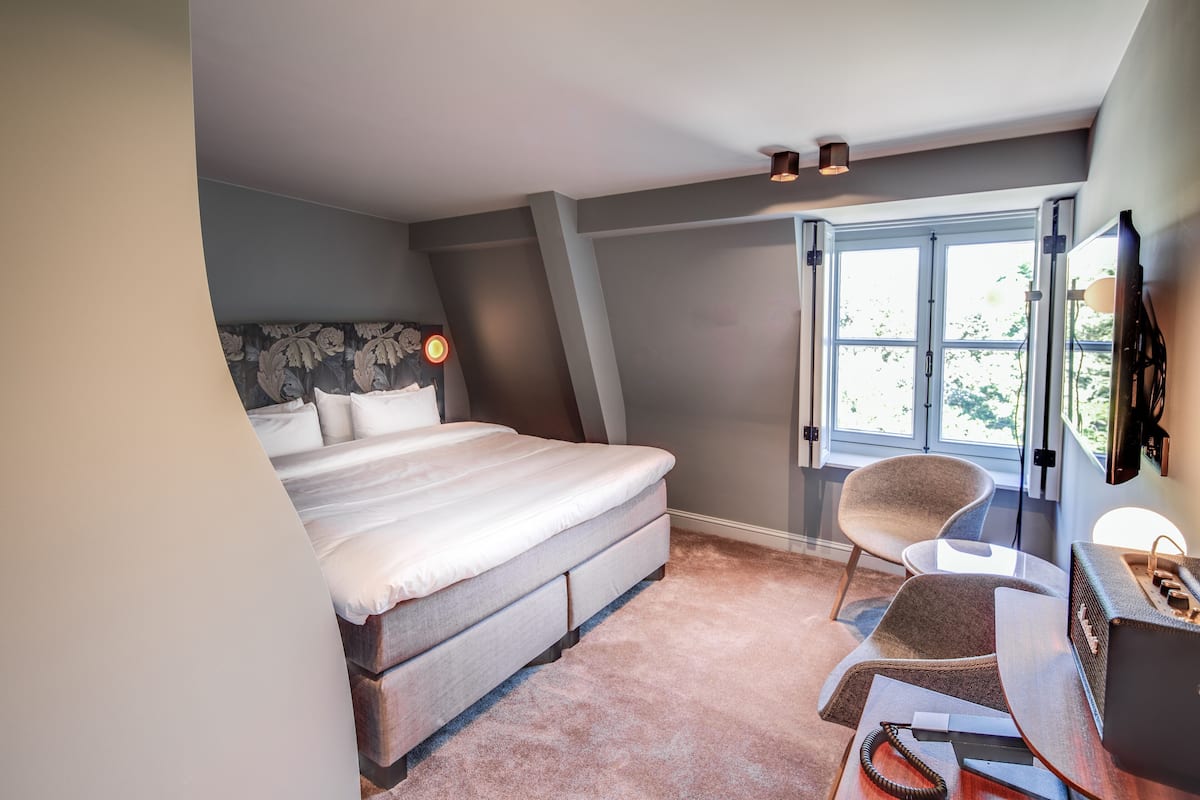 Une chambre à coucher avec un lit, un bureau, une chaise, une fenêtre et une lampe.