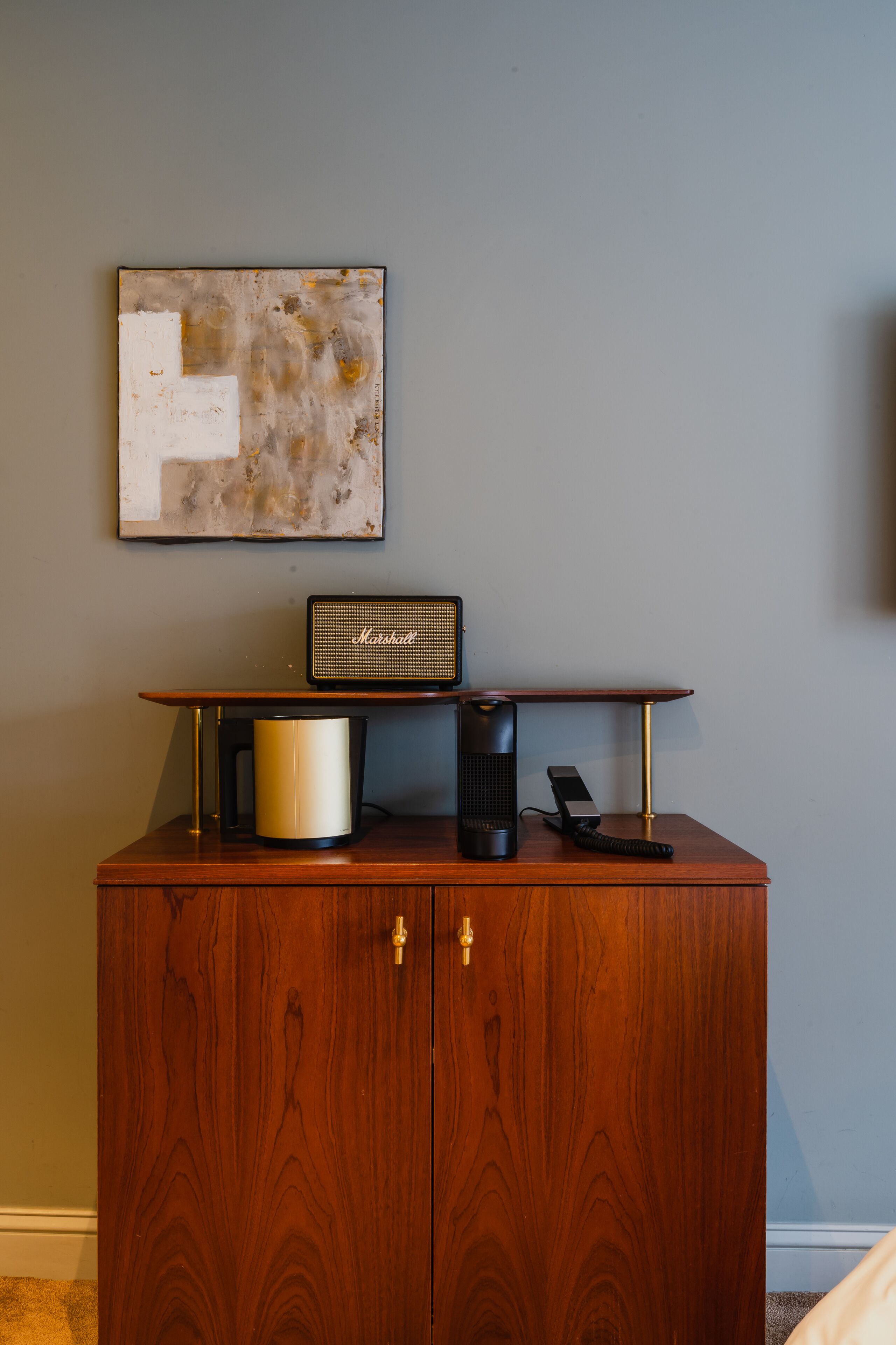A wooden cabinet with a coffee maker, a radio, and a telephone on top.