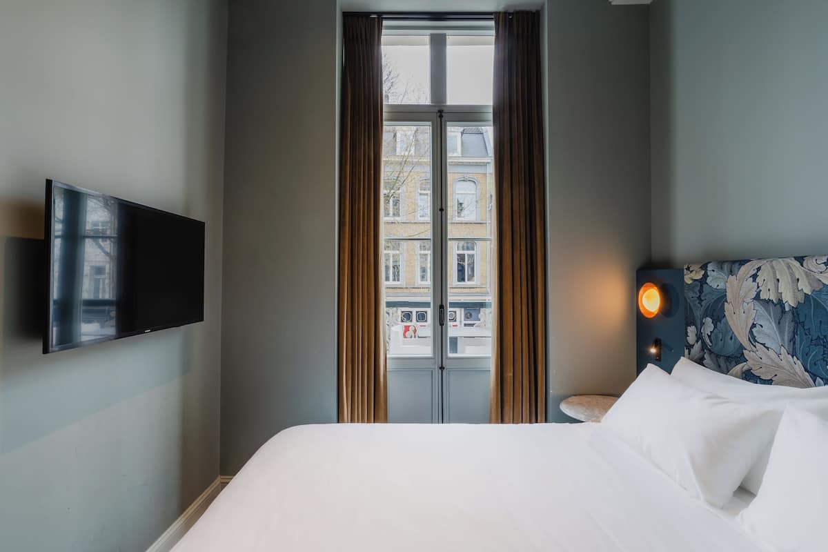 Une chambre d’hôtel équipée d’un lit, d’un téléviseur à écran plat fixé au mur, d’une fenêtre avec des rideaux et d’un luminaire fixé au mur.