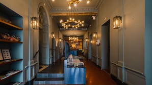 Un hall d’hôtel avec un comptoir d’accueil central, des étagères à livres et un escalier menant aux étages supérieurs.