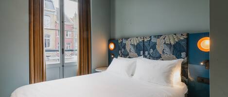 Una habitación de hotel con una cama grande, una ventana con cortinas y una lámpara fijada a la pared.