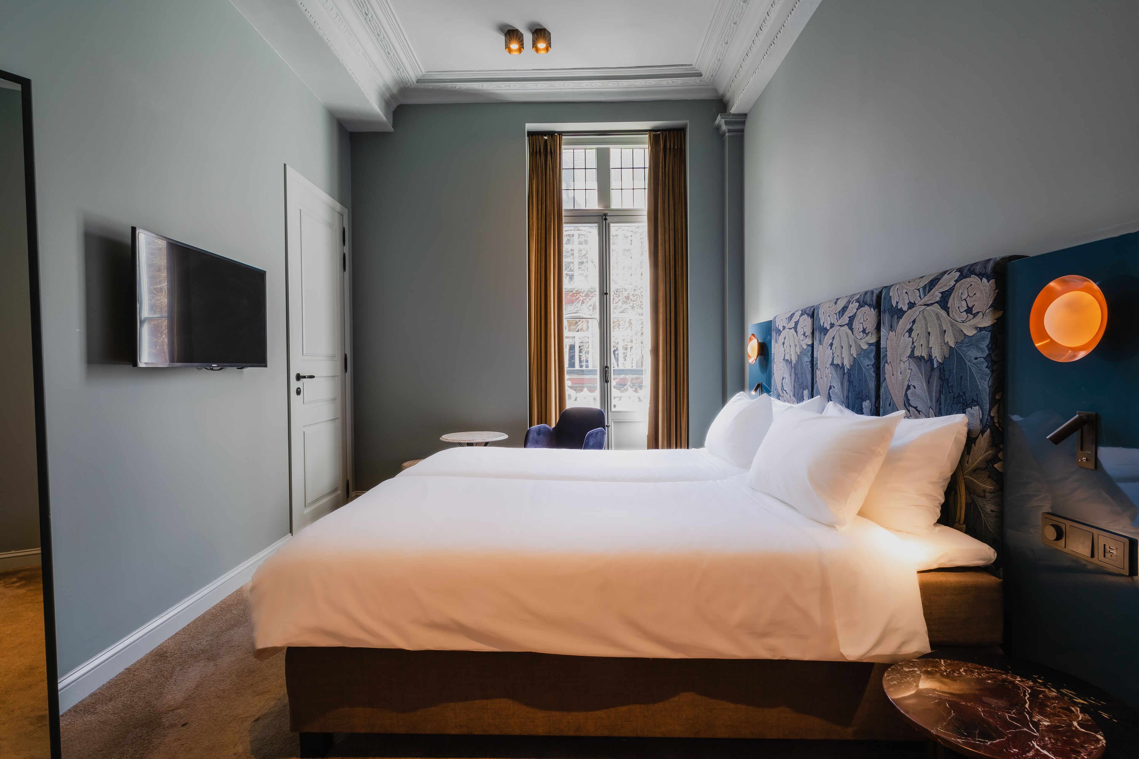 Een hotelkamer met een groot bed, een flatscreen televisie aan de muur, een raam met gordijnen en een decoratief hoofdeinde.