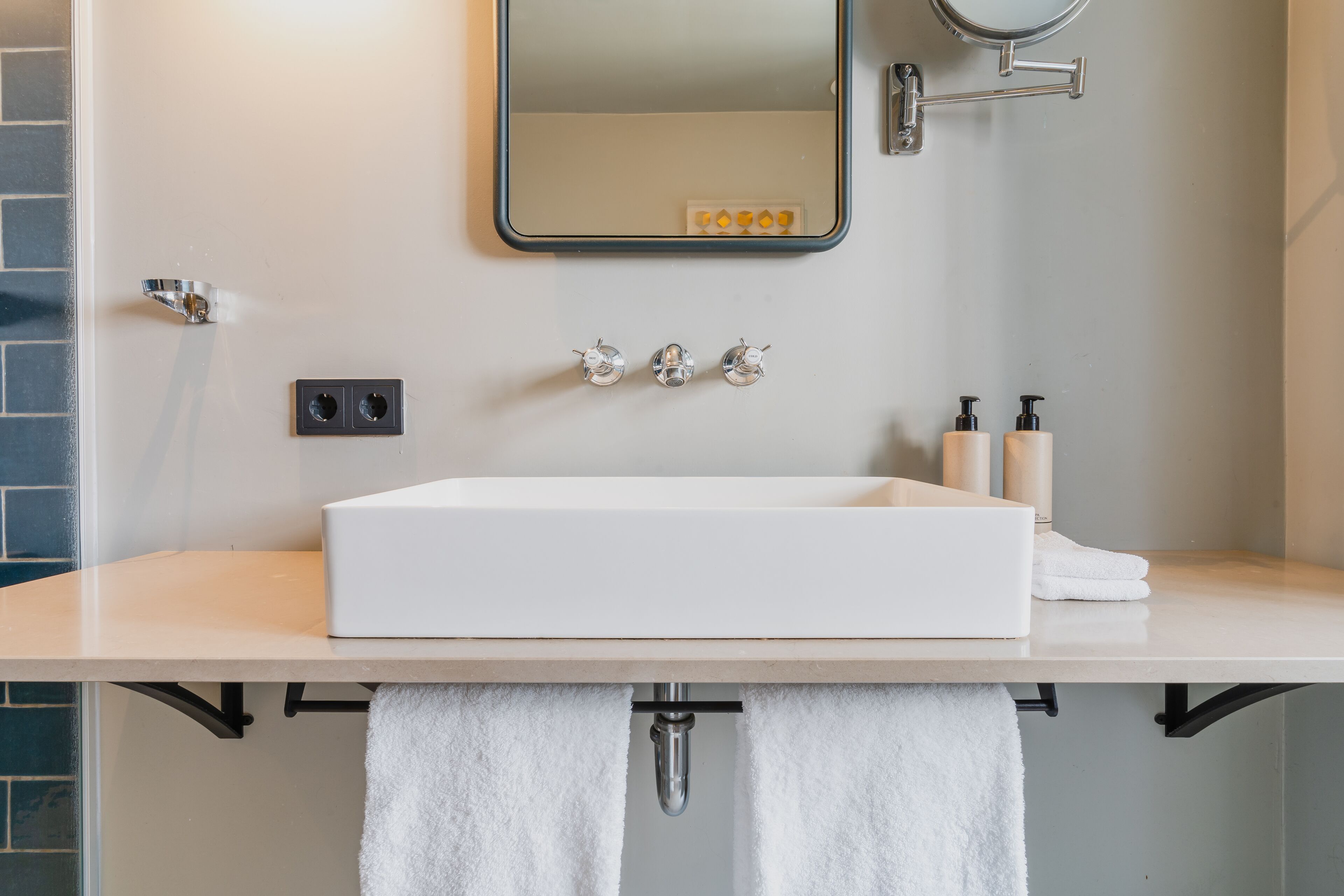 Een badkamer met een witte wastafel, drie kraanwerkstukken, een spiegel en twee zeepdispensers.