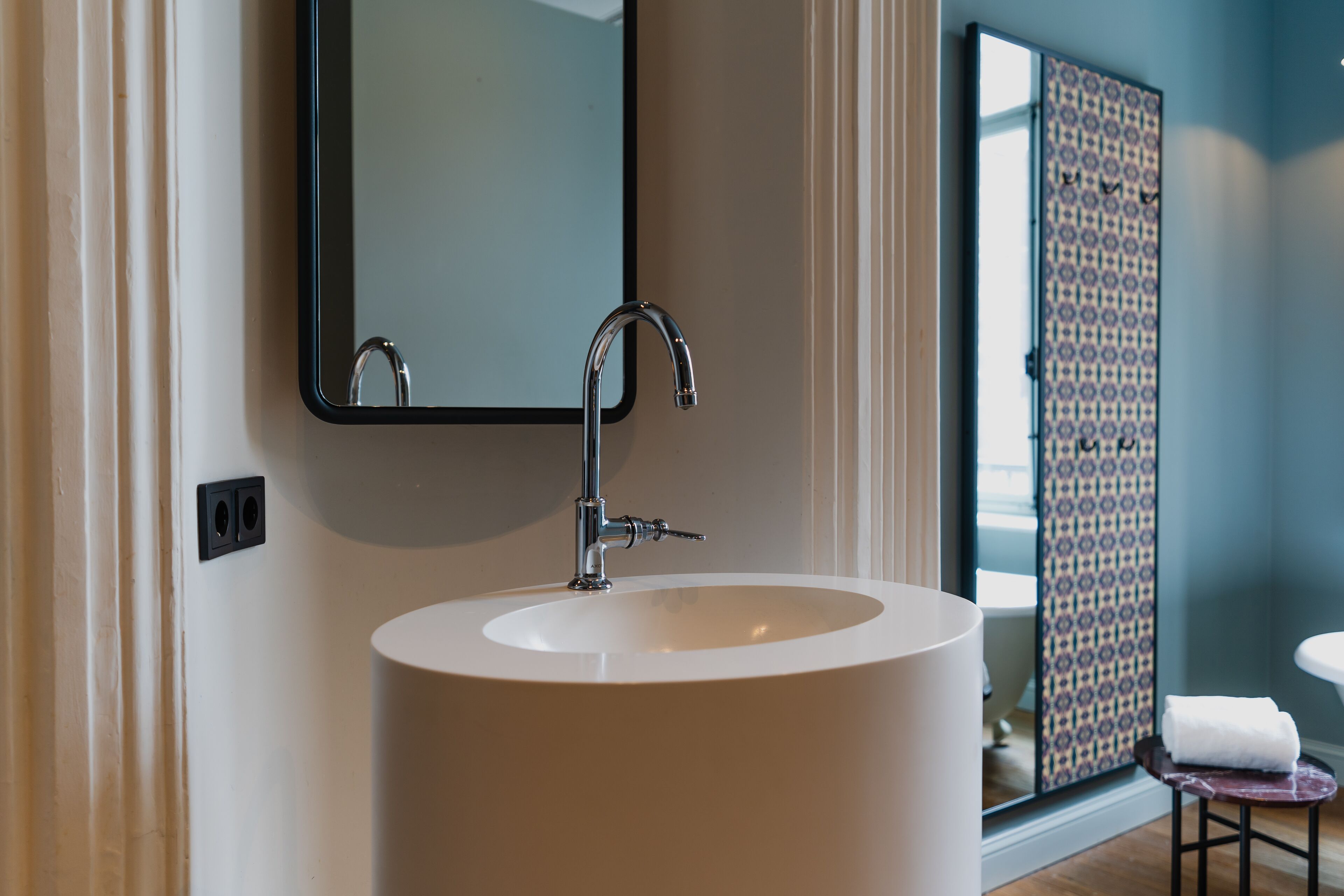 A bathroom with a large white sink, a mirror, and a patterned shower door.