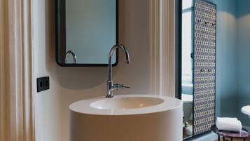 A bathroom with a large white sink, a mirror, and a patterned shower door.