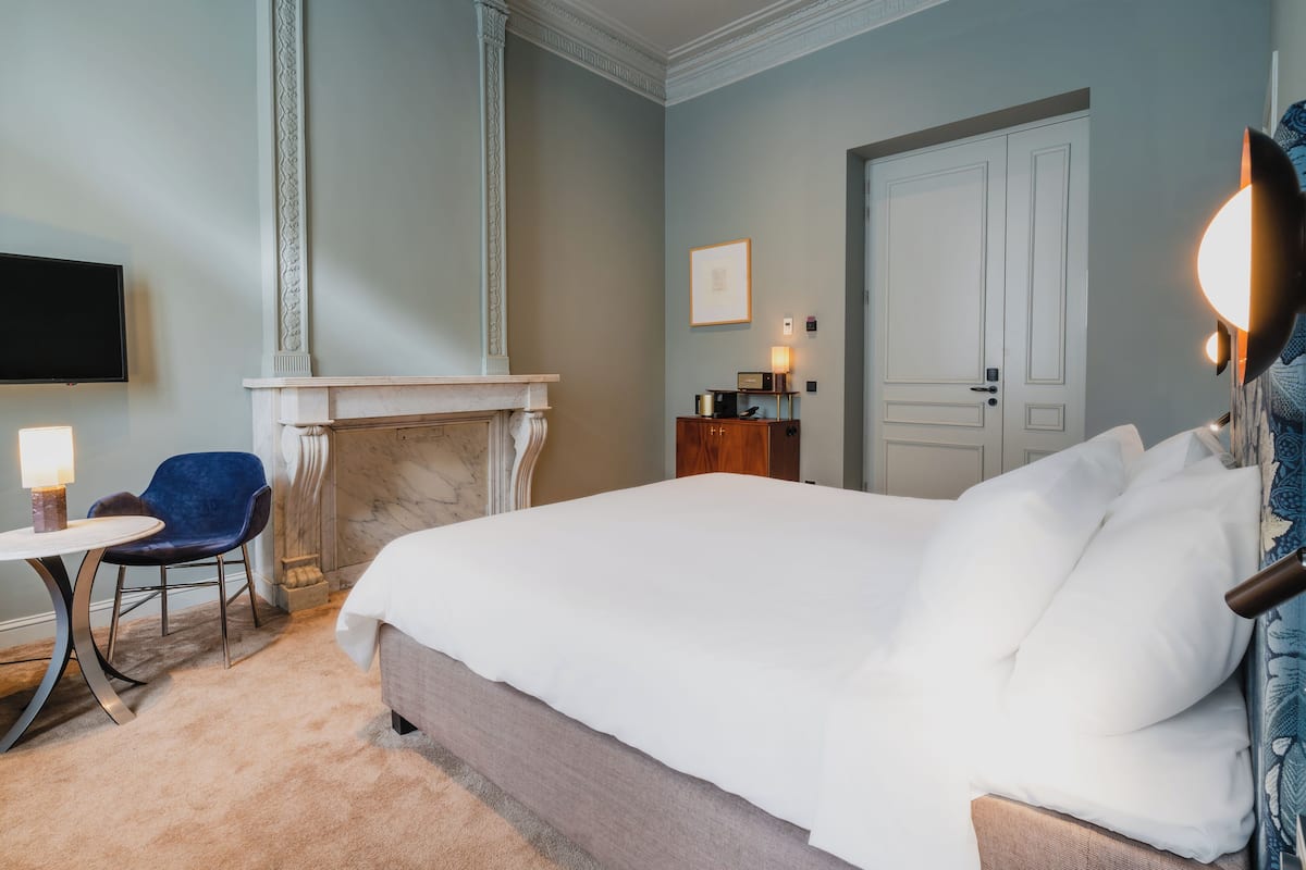 Une chambre d’hôtel avec un grand lit, une cheminée, un bureau avec une chaise et une télévision.