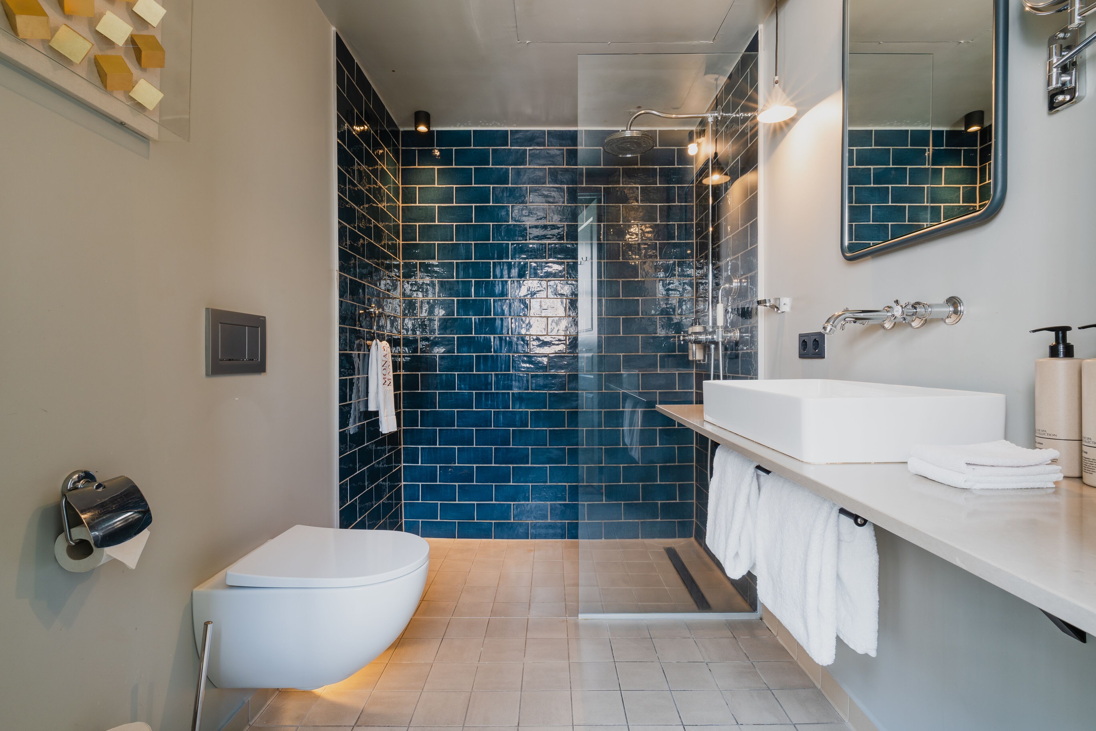 Een moderne badkamer met een wit toilet, een wastafel met spiegel en een douchegedeelte met blauwe tegels.
