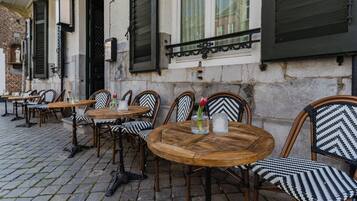 An outdoor cafe with wooden tables and chairs, some with black and white patterned cushions.