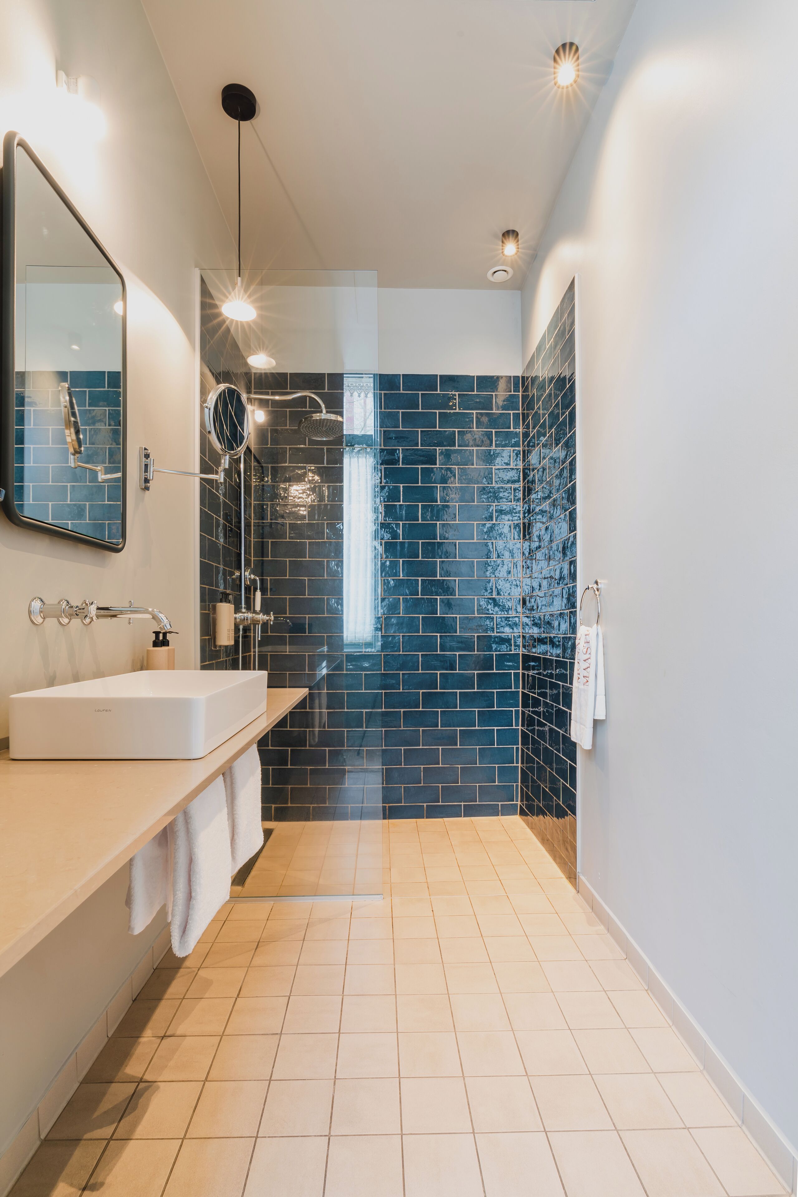 A modern bathroom with a white sink, a mirror, and a shower area with blue tiles.