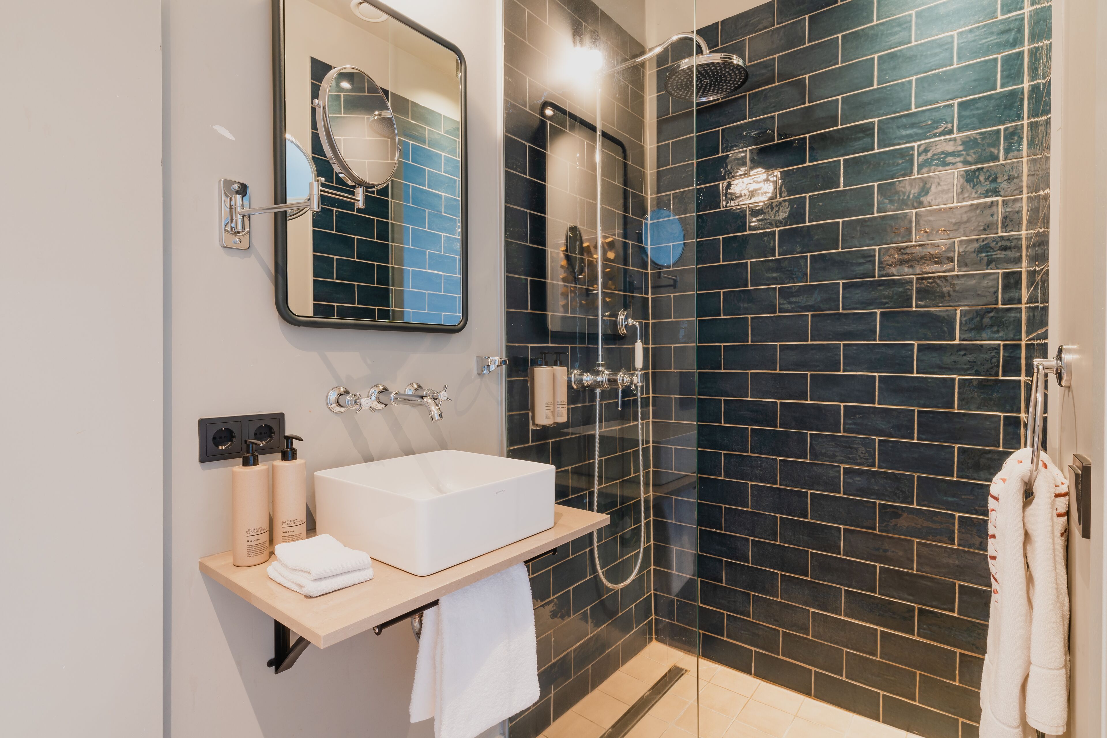 A modern bathroom with a white sink, mirror, and black tiled shower wall.