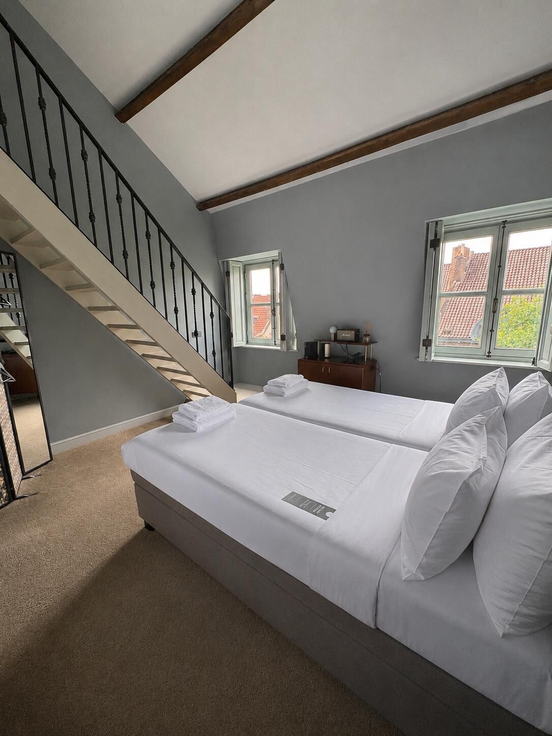 A hotel room with a staircase, two beds, a small table, and a window.