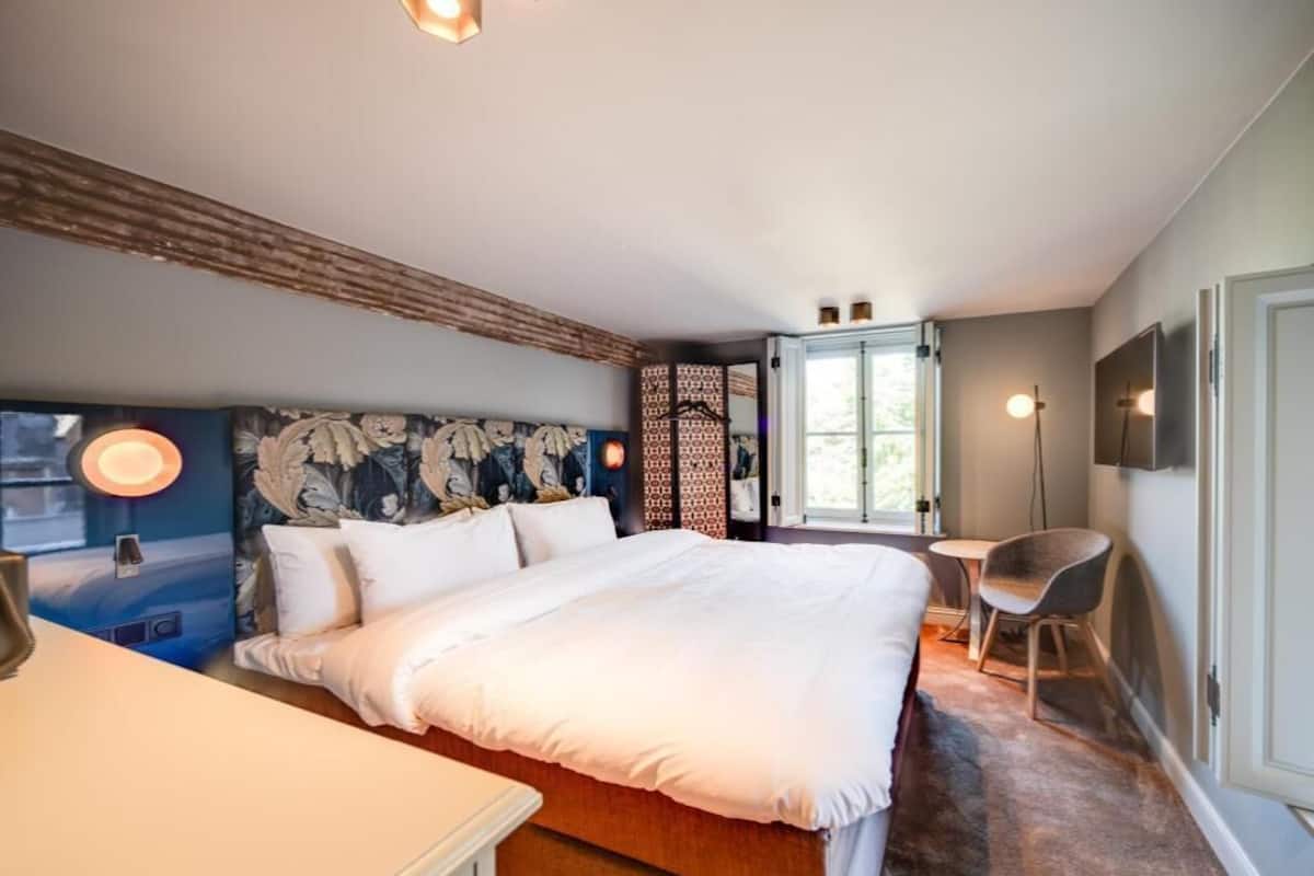 Une chambre à coucher avec un grand lit, un bureau, une chaise, une fenêtre et un téléviseur fixé au mur.