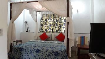 Un dormitorio con cama con dosel, televisor y ventana con cortinas florales.