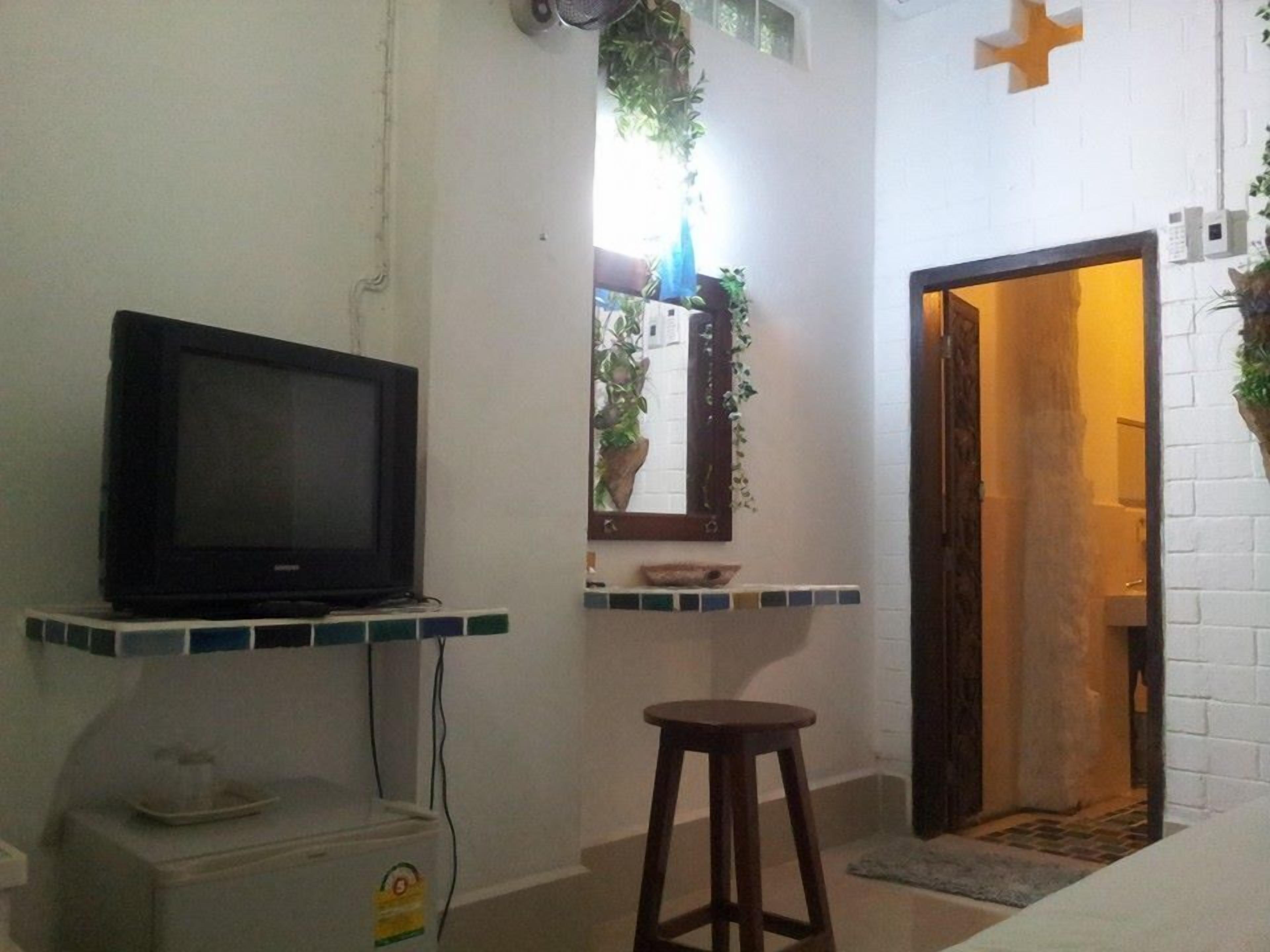 A room with a television on a shelf, a small stool, a tiled floor, and a doorway leading to another room.