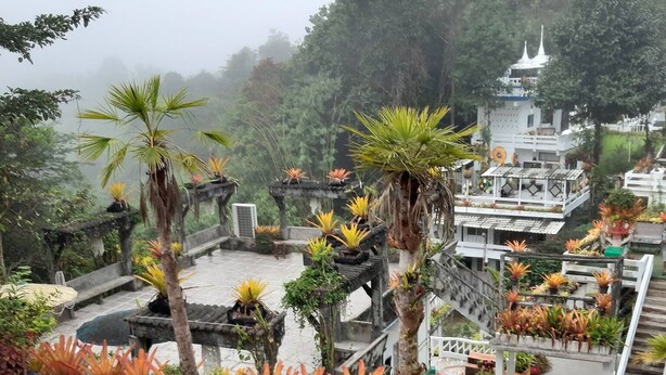 A rooftop garden with seating areas and a view of a temple in the background. - Ban Thor Phan (Sangkhla Buri)
