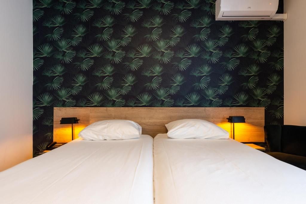 Una cama doble con sábanas blancas, dos lámparas de noche y una pared con diseño de hojas.