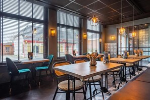 Un interior de restaurante con mesas y sillas, ventanas amplias y lámparas colgantes.