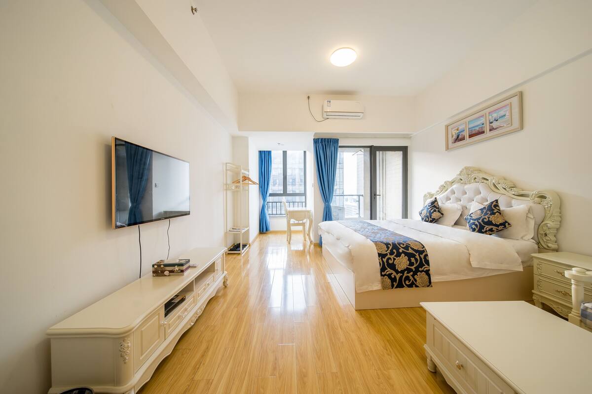 Une chambre bien éclairée, avec un grand lit, une télévision, une commode et un fauteuil.