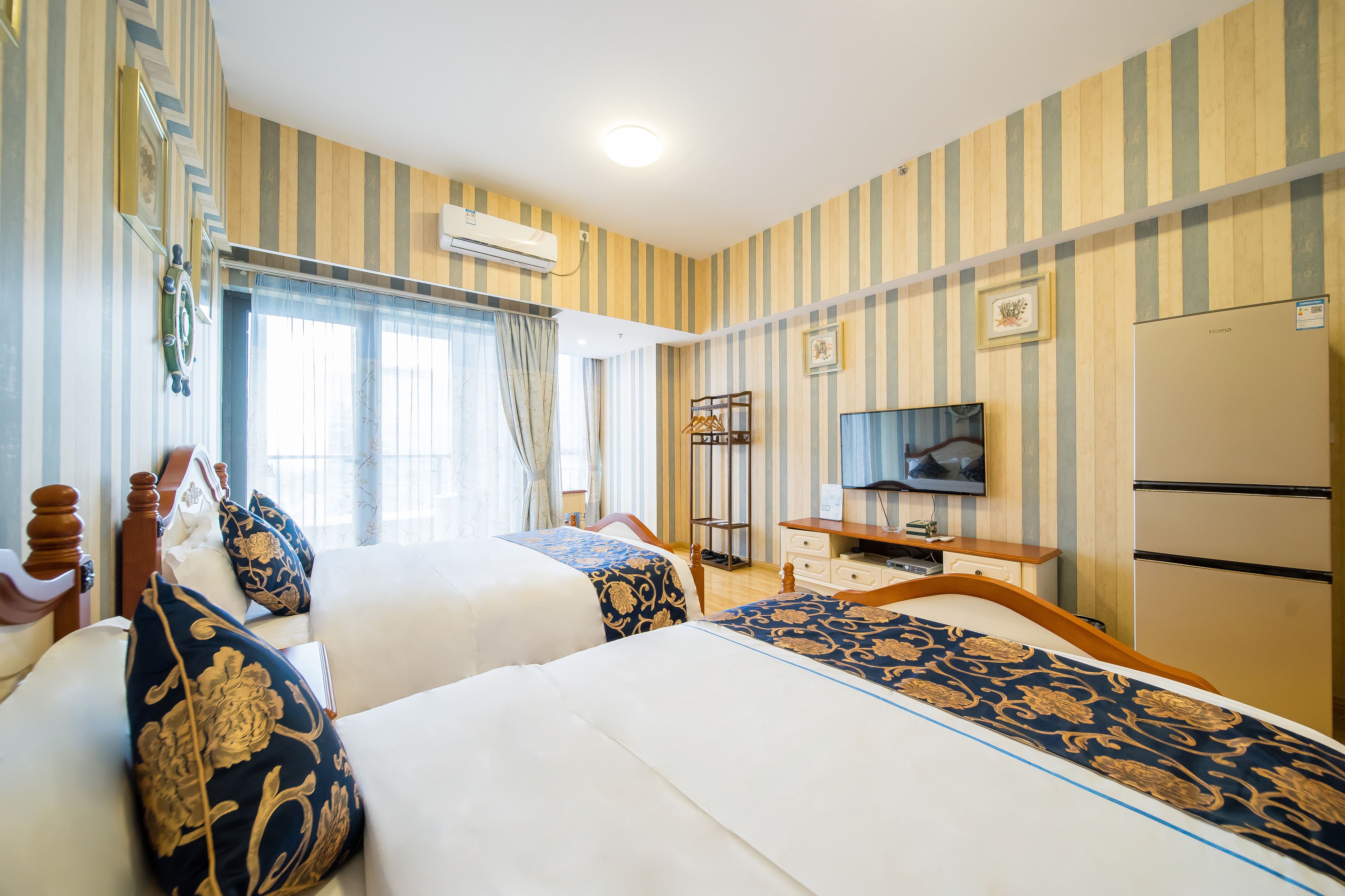 Habitación de hotel con dos camas, televisión, refrigerador y ventana con cortinas.