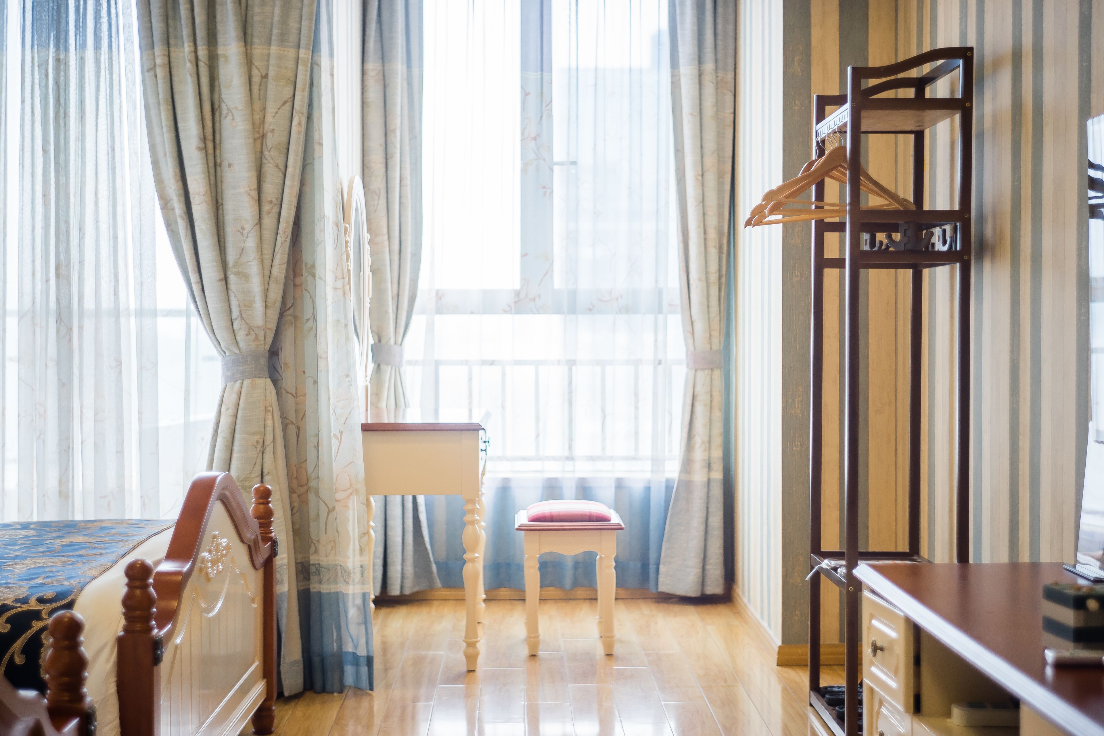 Una habitación de hotel con una cama, una silla de madera, un escritorio y un perchero.