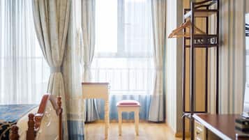Una habitación de hotel con una cama, una silla de madera, un escritorio y un perchero.