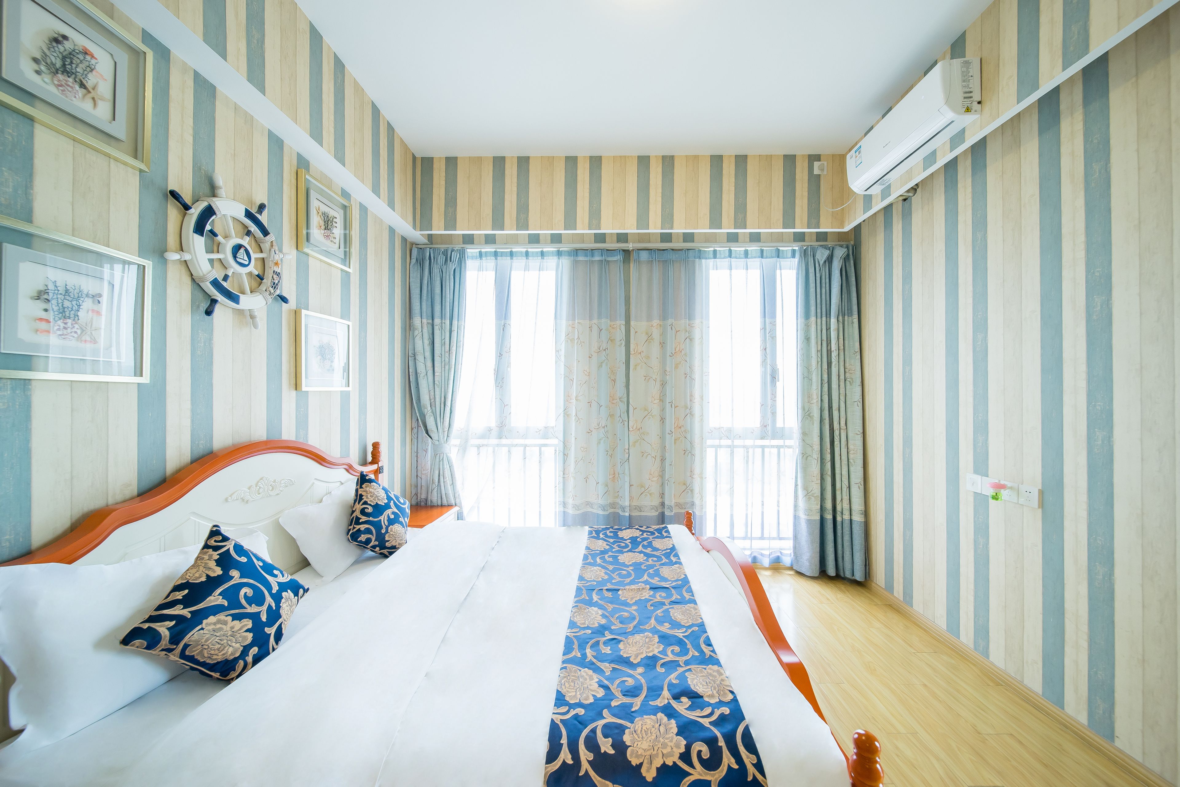 A hotel room with striped wallpaper, a bed with white linens, blue and gold pillows, and a decorative wall hanging.