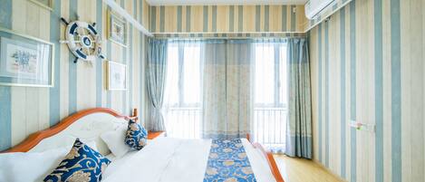 A hotel room with striped wallpaper, a bed with white linens, blue and gold pillows, and a decorative wall hanging.