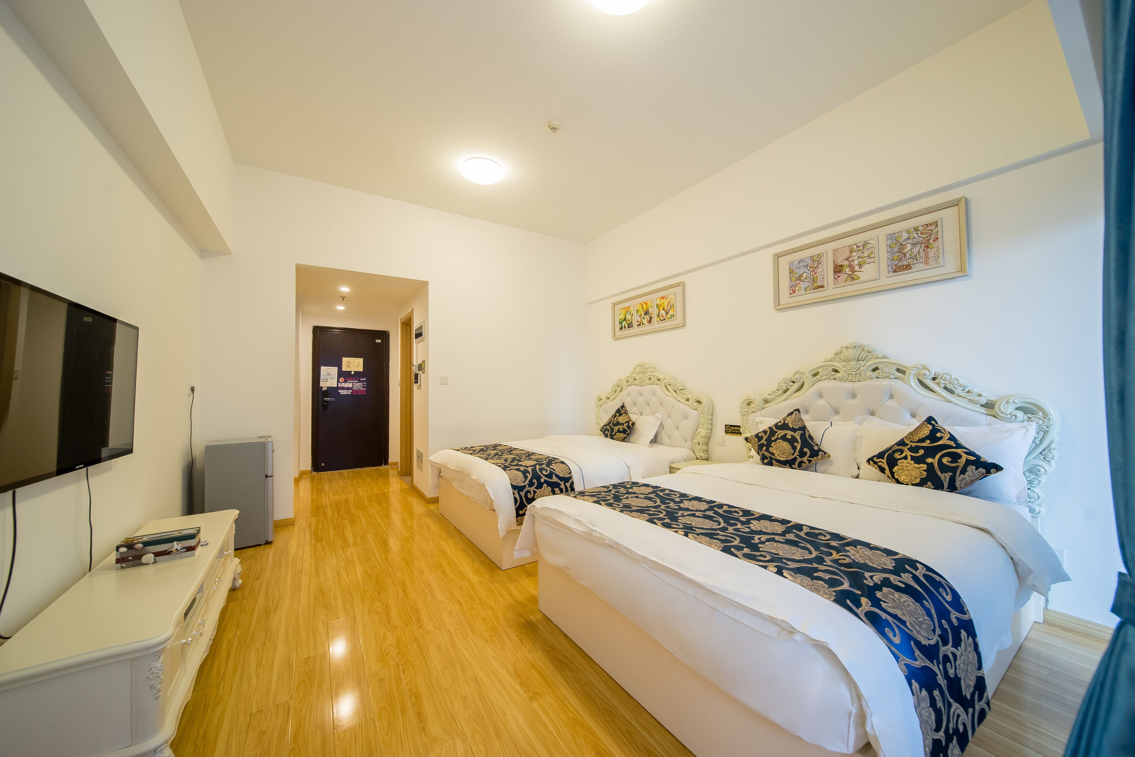 A hotel room with two beds, a TV, a small fridge, and a desk.