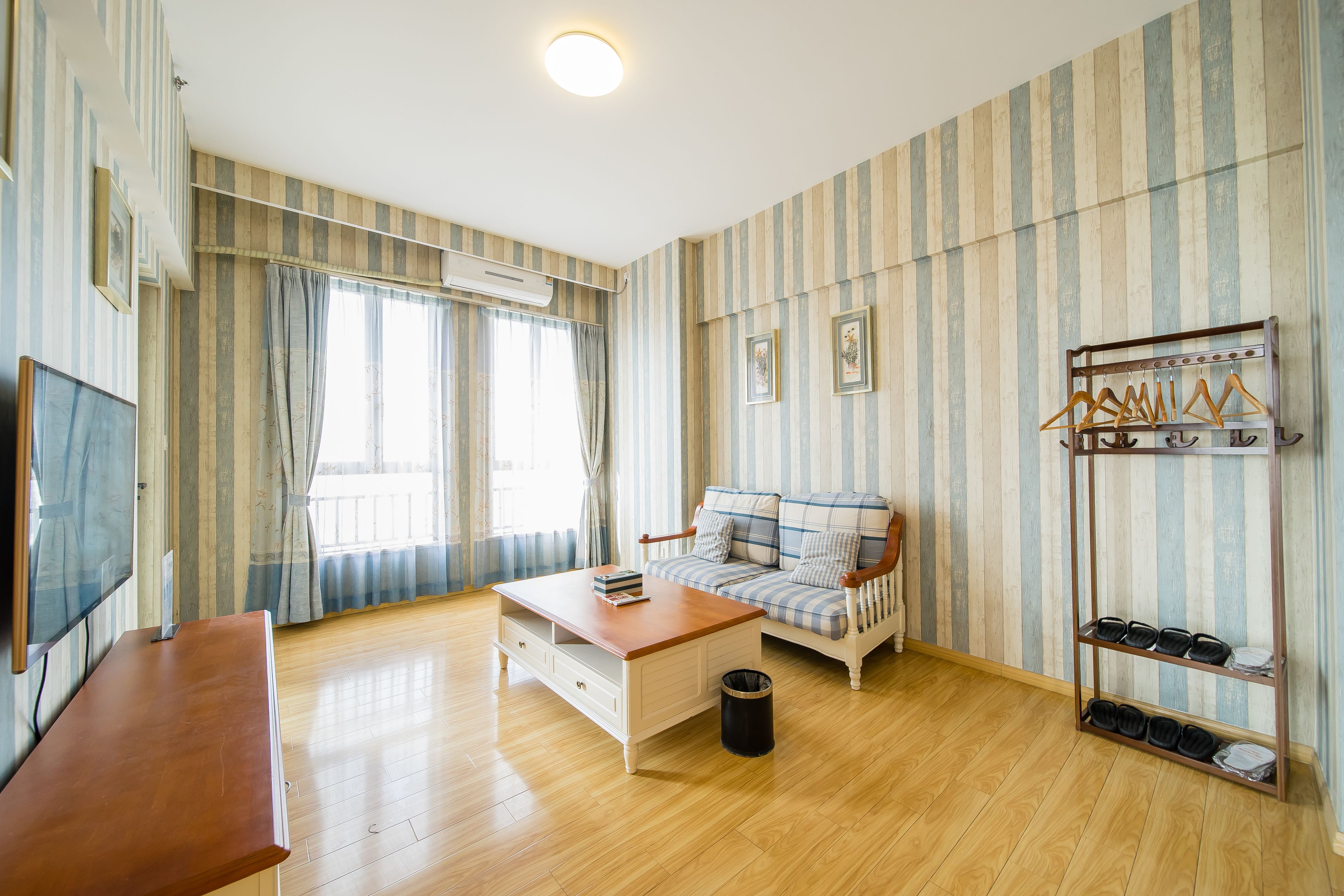 Una habitación con piso de madera, un sofá, una mesa de centro, un televisor y un zapatero.