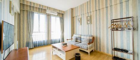Una habitación con piso de madera, un sofá, una mesa de centro, un televisor y un zapatero.