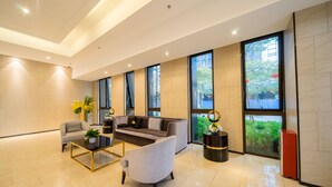 A spacious lobby with a modern sofa, armchairs, and a coffee table. Large windows provide natural light and views of greenery outside.