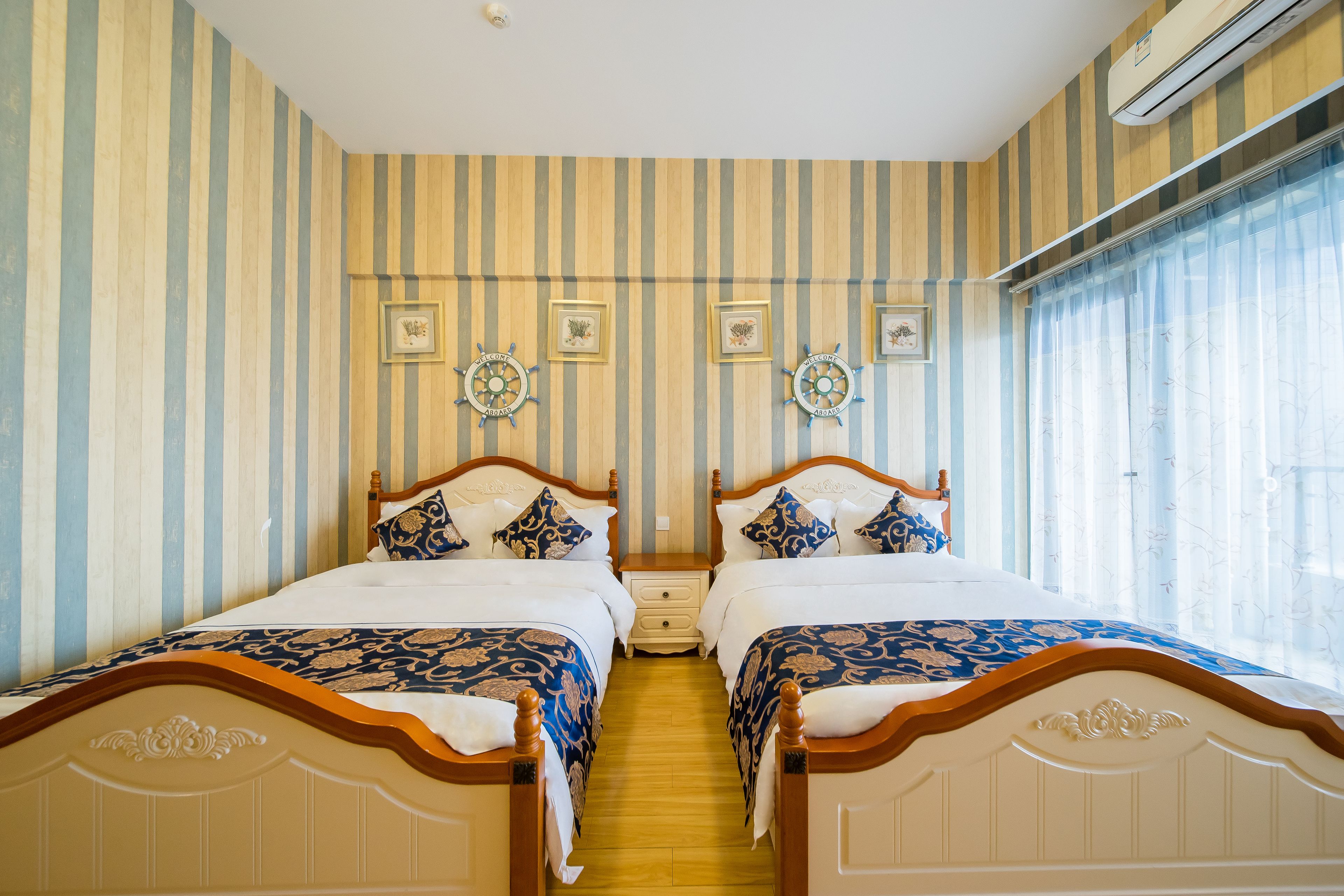 Quarto de hotel com duas camas, papel de parede listrado, relógios decorativos na parede e uma janela com cortinas.