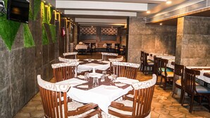 A restaurant with wooden tables and chairs, a patterned wall, and a tiled floor. - Jai Malahar Residency (Panvel)